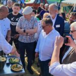 plenerowa impreza, grupa ludzi wokół stołu z daniami kulinarnymi